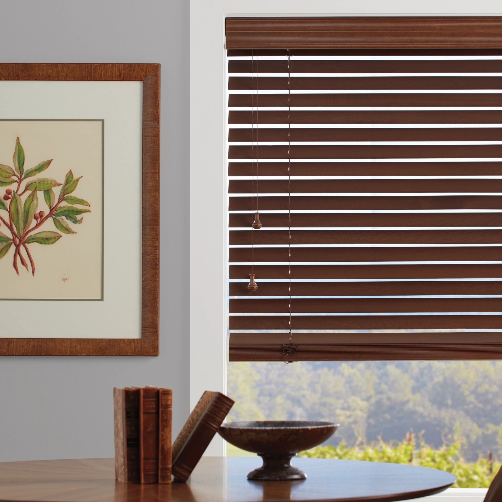 wood blinds tilted slightly open and 75%$ down with table, book and vase.