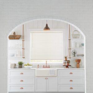 wood blinds tilted closed and 90% down in front of kitchen sink with brass faucet, lighting fixtures and drawers with brass handles, arched entry to kitchen