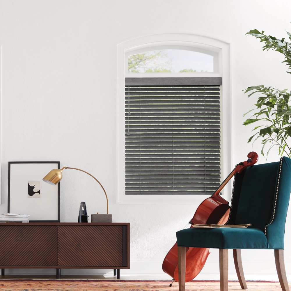 wood blinds tilted closed in the living room with a cello leaning against a chair, storage cabinet lamp, picture and tree by window