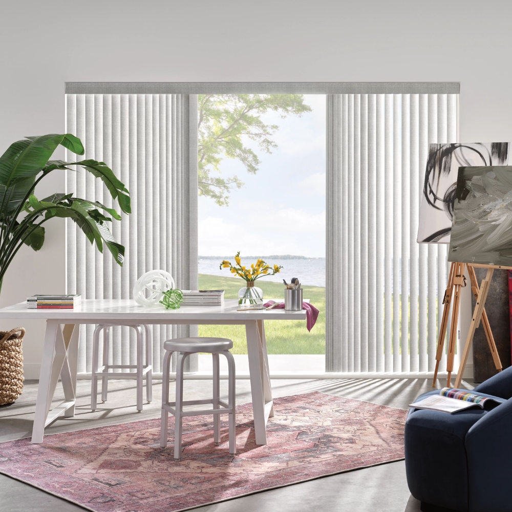 vertical shades stacked on either side of patio window with opening in middle, desk, tall plant and paintings