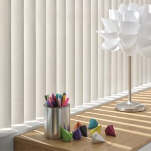 vertical blinds partially open with shows on the table with a holder for colour pencils and colour blocks surrounding it on a table